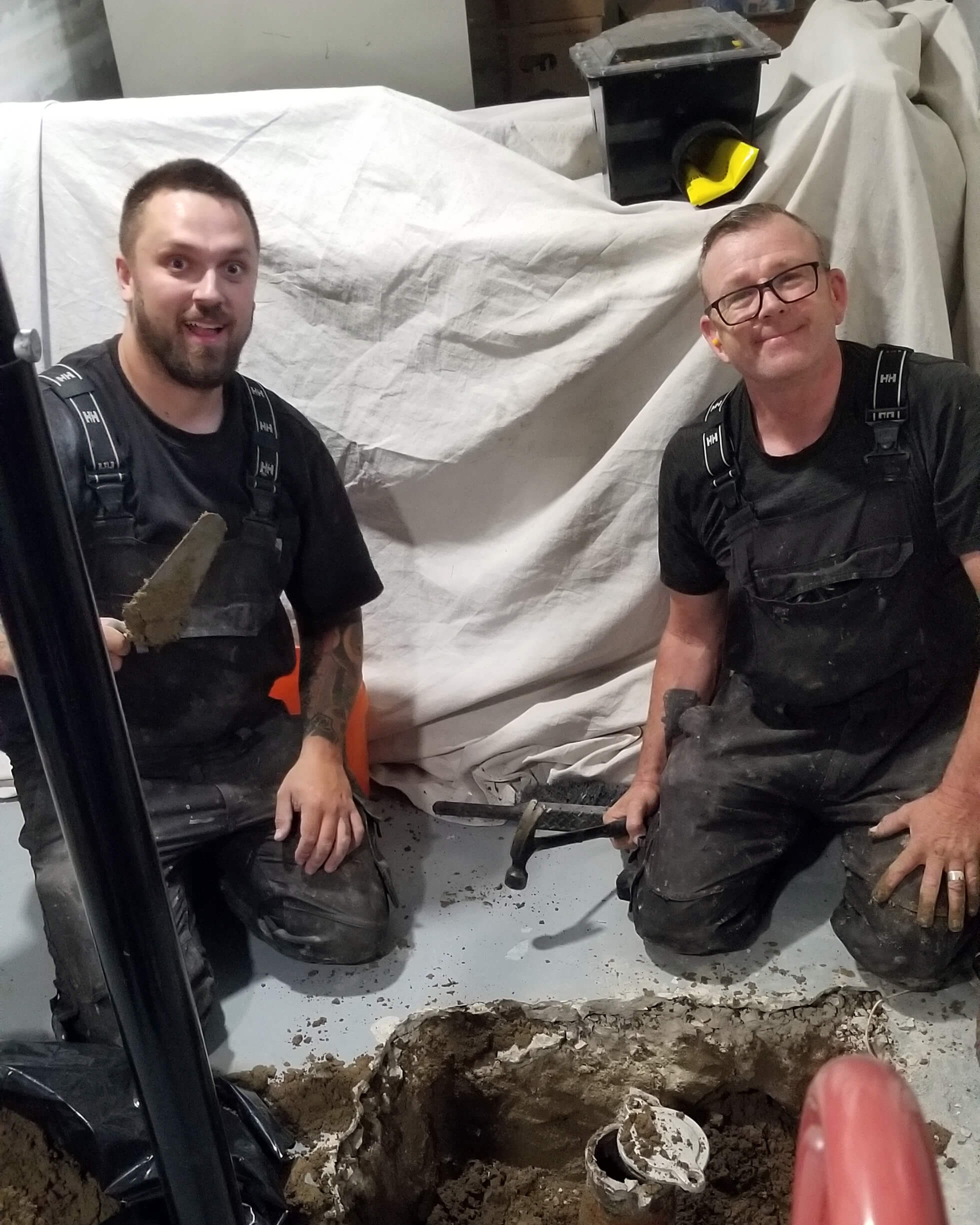 Father and son performing sewer line repair in an Canmore basement, with old cast iron line exposed.