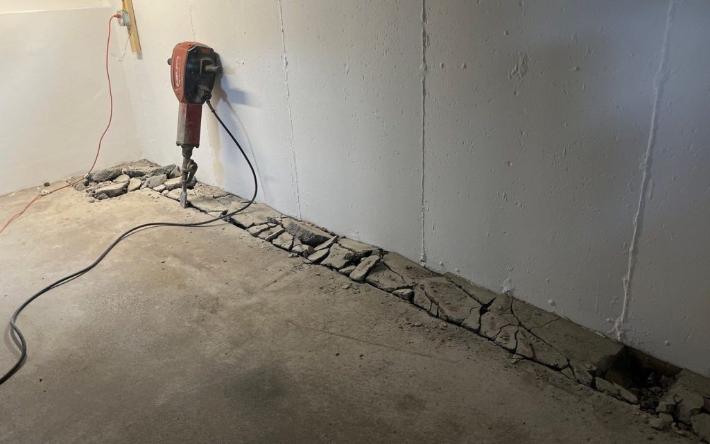 Basement concrete floor trench prepared along the foundation wall for interior French drain installation.
